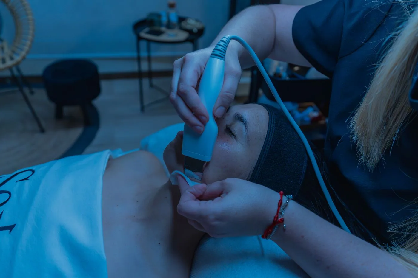 Esteticista aplicando un dispositivo de limpieza sobre el rostro de una paciente durante un tratamiento facial