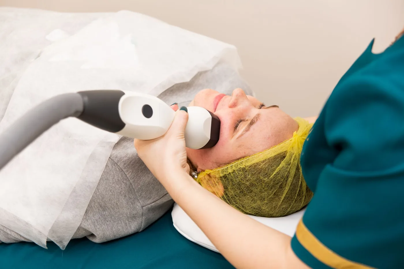 Profesional aplicando un equipo de mano sobre la mejilla de una paciente recostada durante un tratamiento facial